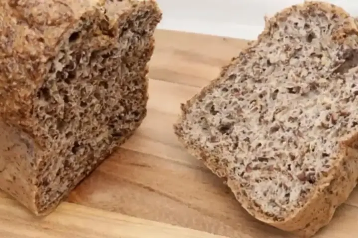 Chleb z siemienia lnianego, pokrojony na desce. Widoczny bochenek i dwa kromki, pełne ziaren.