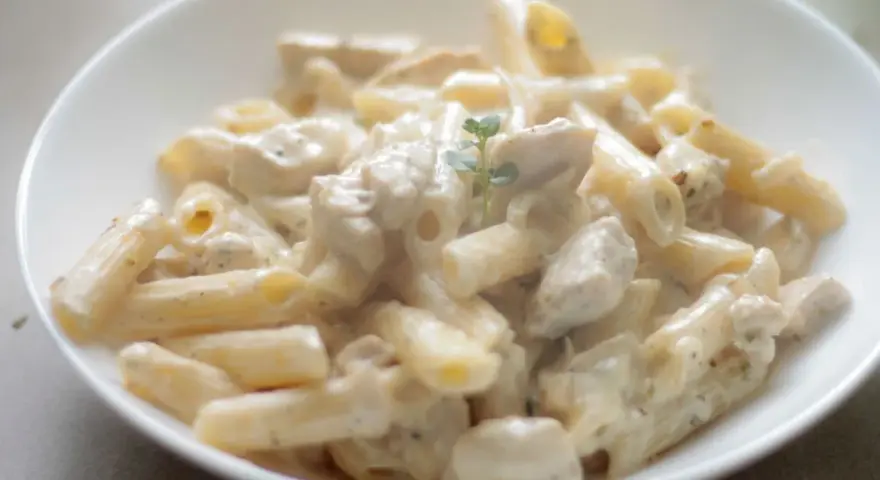 Penne z kurczakiem w kremowym sosie śmietanowo-serowym, udekorowane gałązką ziół. Pyszne danie obiadowe.