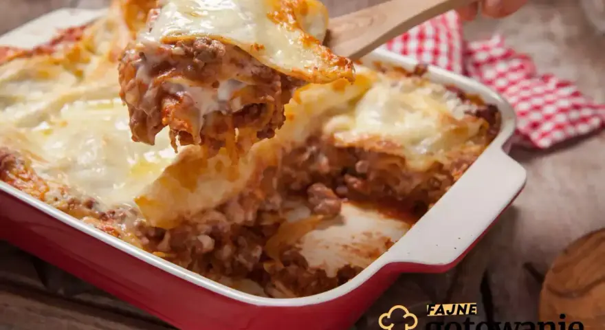 Pyszna, gorąca lasagne z mięsem mielonym i ciągnącym serem, właśnie nakładana drewnianą łopatką. Idealna na rodzinny obiad.