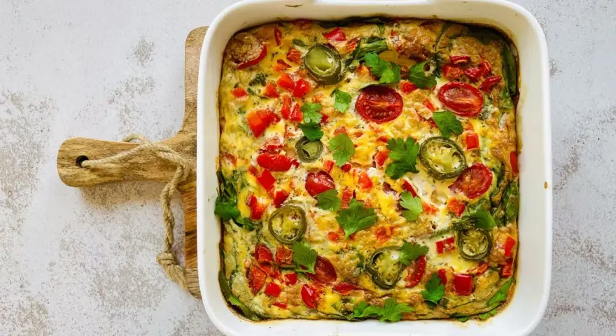 Pyszny omlet z piekarnika z pomidorkami, papryką i jalapeño, udekorowany natką pietruszki.