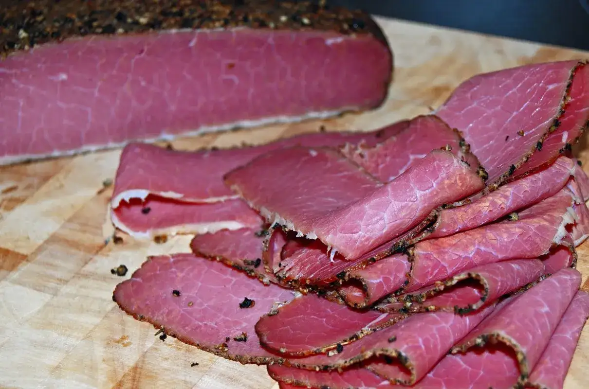 Pokrojone plastry pastrami, co to jest? Aromatyczne, różowe mięso wołowe z pieprzem na desce.