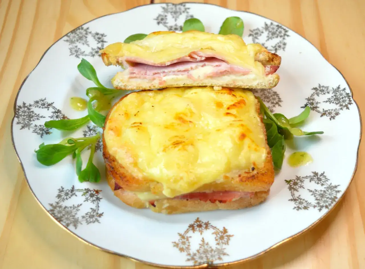 Pyszny croque madame z rozpływającym się serem i szynką, podany z zieloną sałatką na ozdobnym talerzu.