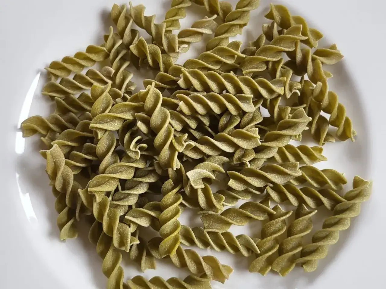 Zielony makaron fusilli z zielonego groszku, ułożony na białym talerzu.