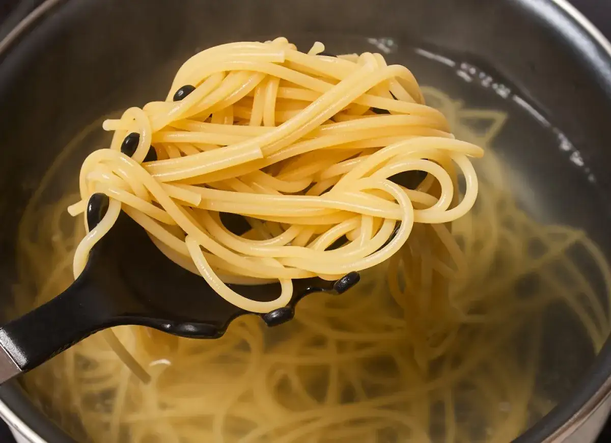 Łyżka do makaronu wyciąga ugotowany spaghetti z garnka. Idealny sposób, jak ugotować makaron al dente.
