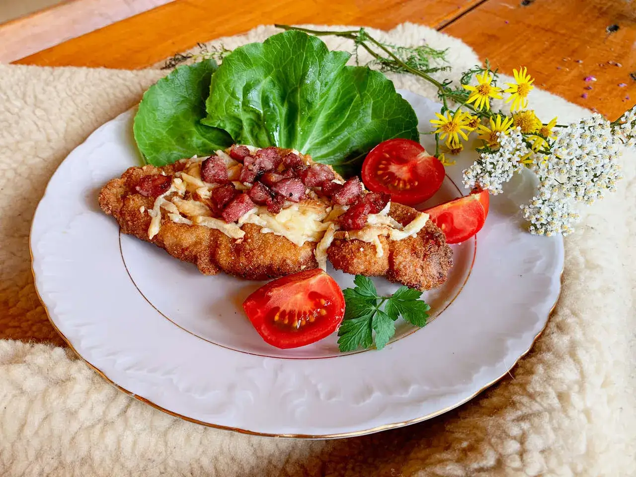 Kotlet schabowy z serem i boczkiem, podany z pomidorami i sałatą. Pyszny obiad, choć warto sprawdzić kotlet schabowy kcal.