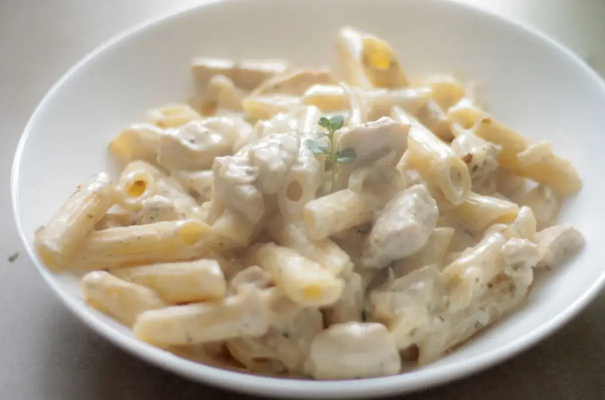 Penne z kurczakiem w kremowym sosie śmietanowo-serowym, udekorowane gałązką ziół. Pyszne danie obiadowe.