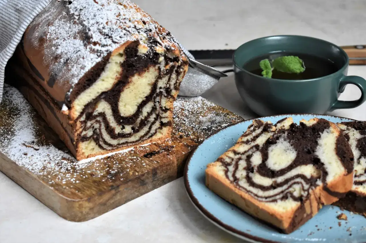Wilgotne ciasto zebra z cukrem pudrem, pokrojone na kawałki, obok filiżanka herbaty z miętą.