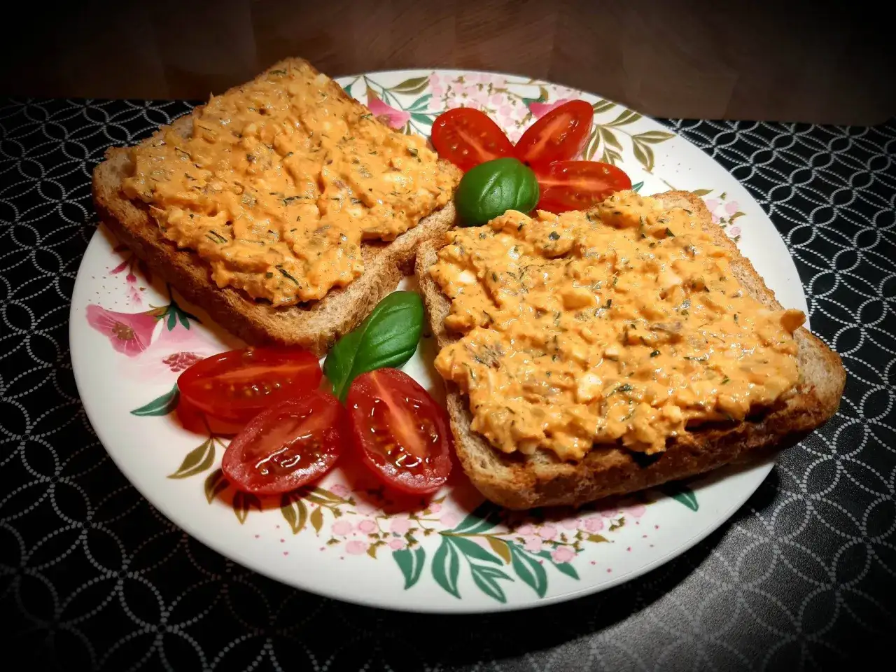 Dwa tosty z pyszną pastą z makreli w pomidorach, ozdobione pomidorkami koktajlowymi i bazylią.