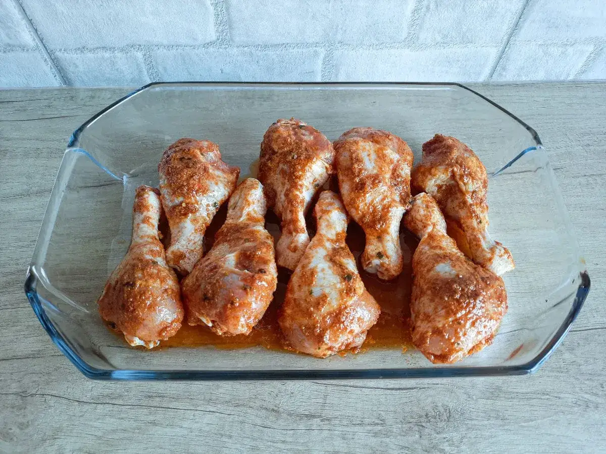 Pałki z kurczaka w szklanym naczyniu, gotowe do pieczenia. Widać na nich aromatyczną marynatę do pałek z kurczaka.