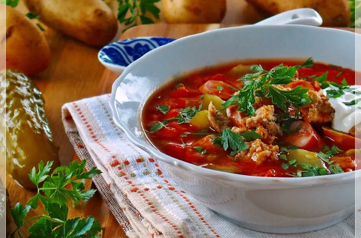 Gęsta, aromatyczna solanka z kiełbasą, ziemniakami i ogórkiem kiszonym, udekorowana natką pietruszki i śmietaną.