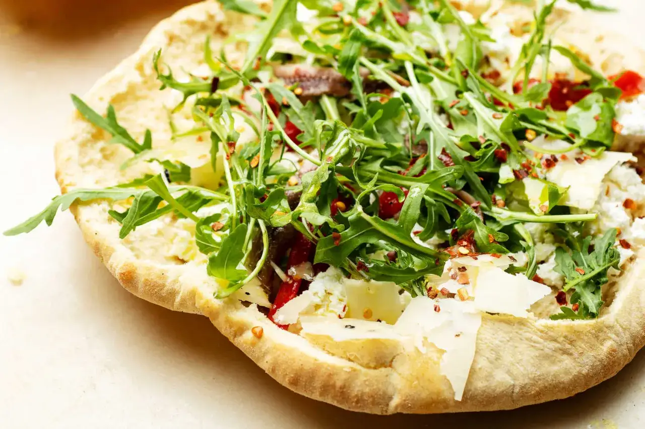 Pyszna pizza bianca z rukolą, serem i anchois, posypana płatkami chili.