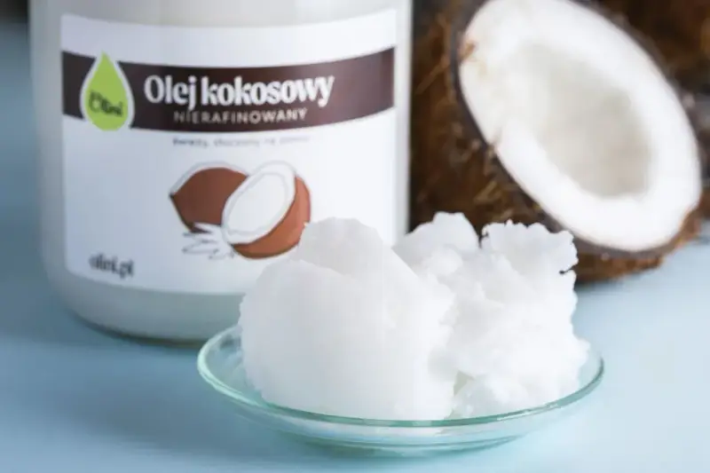 Olej kokosowy nierafinowany, idealny jako zdrowy olej do smażenia. W tle widać połówkę kokosa i słoik z etykietą.