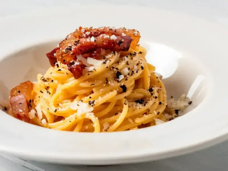 Spaghetti carbonara – przepis oryginalny ze śmietaną. Pyszne danie z makaronem, boczkiem i parmezanem, posypane świeżo mielonym pieprzem.