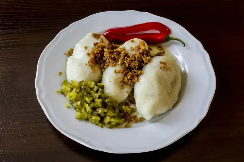 Trzy ziemniaczane kartacze z okrasą, posypane skwarkami, podane z ogórkiem kiszonym i papryczką chili.
