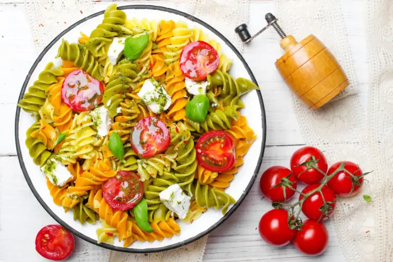 Kolorowy makaron z zielonego groszku, pomidorkami koktajlowymi i fetą, polany pesto.
